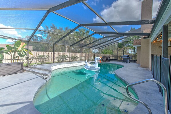 Une piscine extérieure couverte, agrémentée d’une décoration en forme de cygne, entourée d’une clôture en bois et dotée d’un espace barbecue.