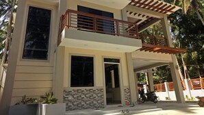 A modern two-story house with a balcony, large windows, and a tiled entrance.