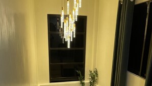 A staircase with a wooden handrail, a modern chandelier, a potted plant, and a window with dark curtains.