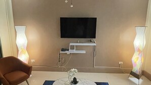A modern living room with a flat-screen TV mounted on the wall, a ceiling fan, a coffee table with a vase, and two floor lamps.