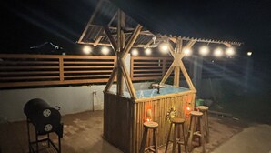 An outdoor bar area with a wooden structure, stools, and a pool table.