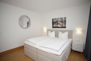 A bedroom with a bed, a round mirror, a nightstand, and a wall-mounted light. - Close to the beach with a terrace; access to the pool and sauna - Strandhaus Mönchgut FeWo06 (Middelhagen)