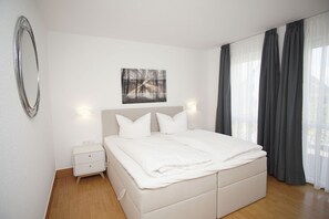 Une chambre à coucher moderne avec un grand lit, une table de chevet, un miroir fixé au mur et un tableau au-dessus du lit.
