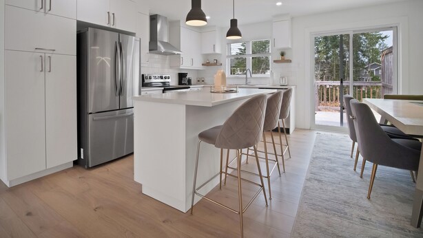 A modern kitchen with white cabinetry, stainless steel appliances, and a central island with bar stools. - Cheerful, modern 3 -bedroom house (Moncton)
