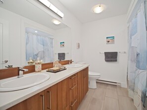 A modern bathroom with a large mirror, two sinks, a toilet, and a shower curtain. - Cheerful, modern 3 -bedroom house (Moncton)