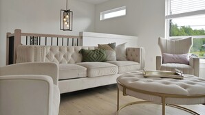 A modern living room with a beige sectional sofa, a round ottoman, a high-back armchair, and a pendant light. - Cheerful, modern 3 -bedroom house (Moncton)