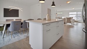 A modern kitchen with white cabinetry, a central island, and pendant lighting. - Cheerful, modern 3 -bedroom house (Moncton)