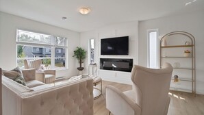 A modern living room with a large flat-screen TV, comfortable seating, and a view of the outside. - Cheerful, modern 3 -bedroom house (Moncton)