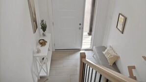 A hallway with a white door, a small table with a plant, and a cushioned bench. - Cheerful, modern 3 -bedroom house (Moncton)