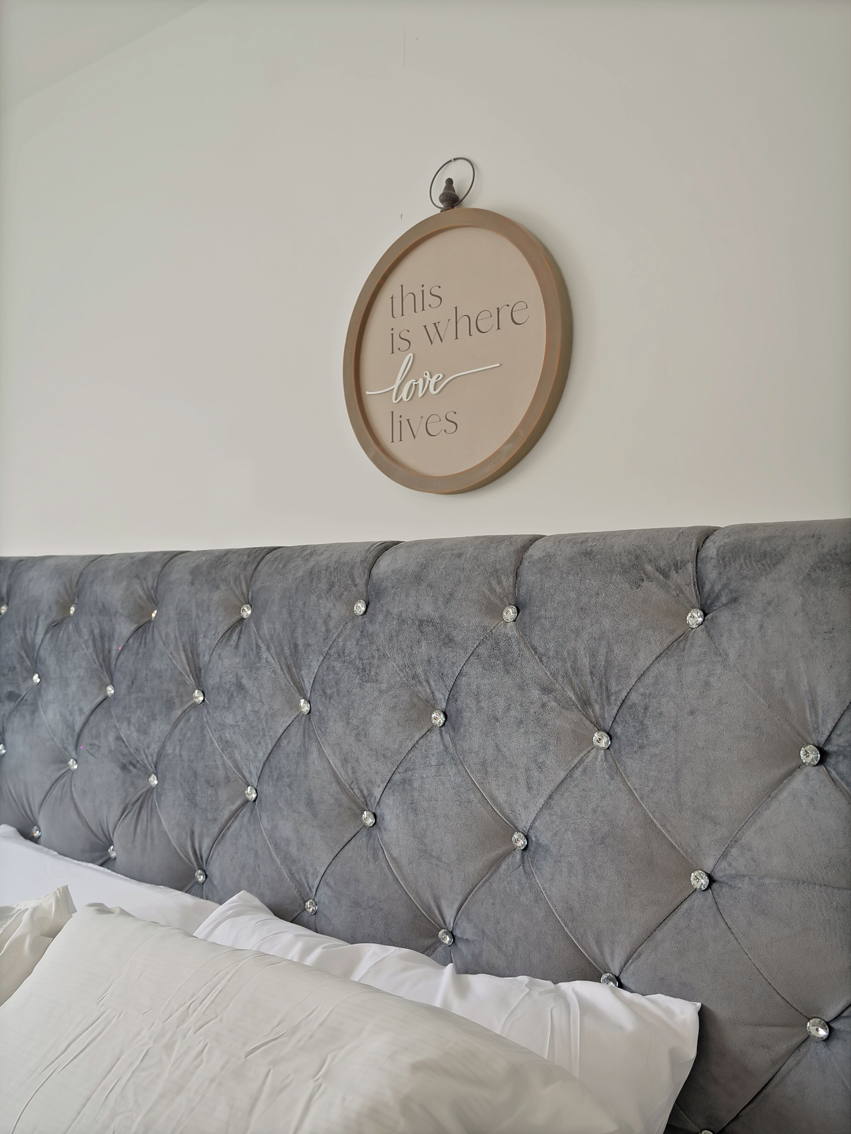 A tufted grey headboard with a decorative sign above it.