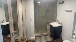 Moderni kylpyhuone, jossa on lasiseinällä varustettu suihku, valkoinen pesuallas ja wc.
