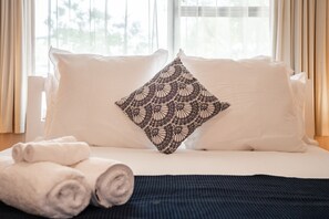 A neatly made bed with white linens and a decorative black and white patterned pillow.
