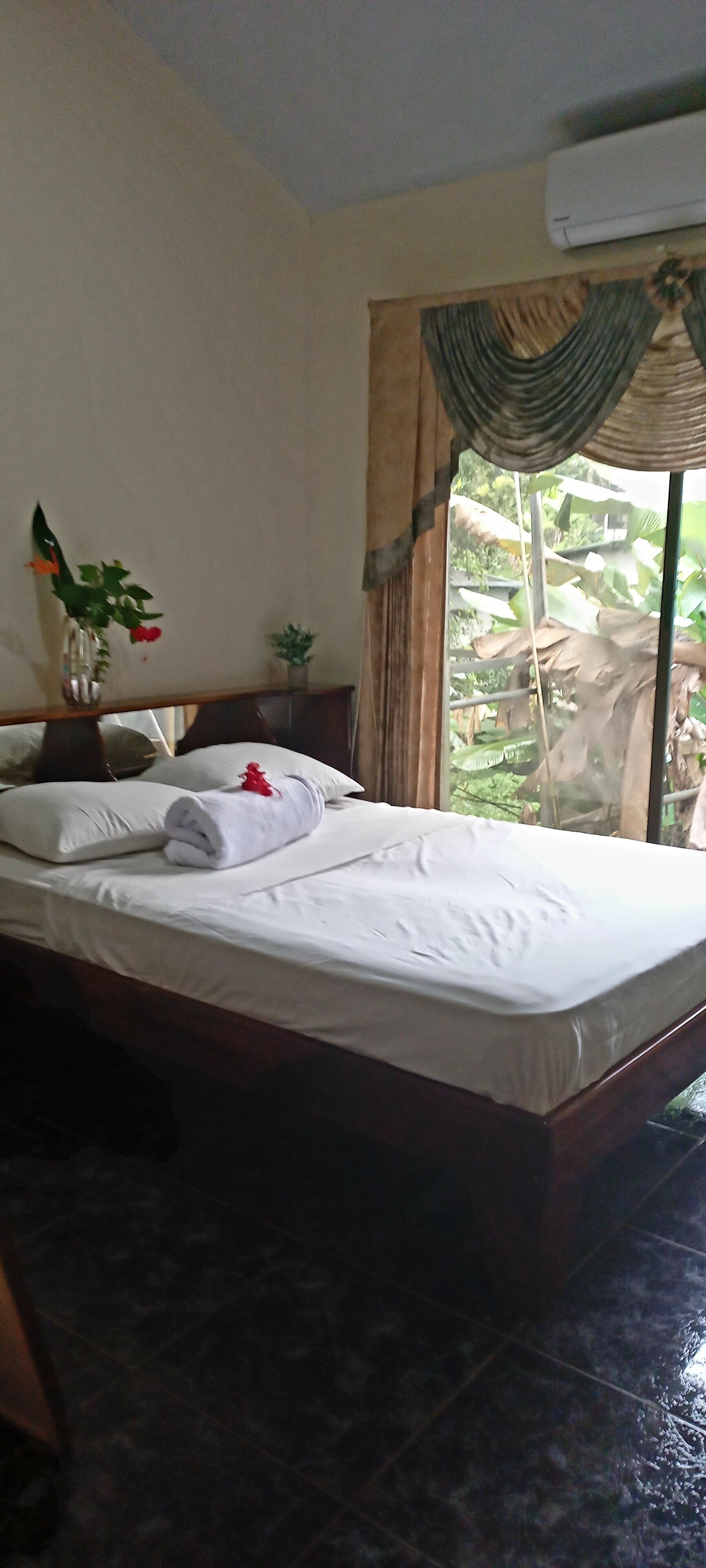 Una habitación de hotel con una cama, una mesita con un florero y una ventana con cortinas.