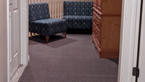 Un pasillo con alfombra, dos sillas estampadas y un mueble de madera.