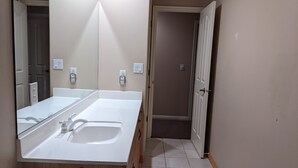 Un baño con un espejo grande, un lavamanos blanco y una puerta de ducha.