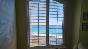 A room with a large window overlooking a beach and a pier. There is a wooden table with a telescope and decorative items. - 7th floor 2 bedroom 2 bath oceanfront condo at Beach Colony West. (Navarre)