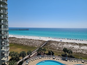 A beachfront hotel with a pool, beach umbrellas, and a pier.