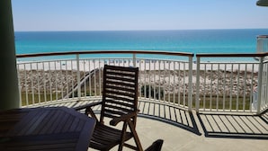 A balcony with a wooden chair and table, overlooking a beach with a clear view of the ocean. - 7th floor 2 bedroom 2 bath oceanfront condo at Beach Colony West. (Navarre)