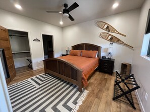A bedroom with a wooden bed, a ceiling fan, a nightstand, a lamp, a wicker chair, and a window. - NEW Cabin in Terry Peak!  Views, Space, and lots more!  Sleeps 14, NO bunk beds! (Lead)