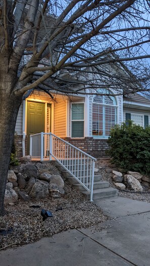Una casa residencial con un porche delantero, una escalera que lleva a la puerta y un jardín con rocas y un árbol.