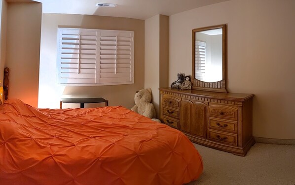 Un dormitorio con una cama grande, un aparador, un espejo y una ventana con persianas.