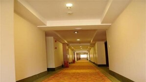 Ein langer, schmaler Hotelkorridor mit einem gemusterten Teppich, weißen Wänden und einer Decke mit Einbauleuchten.