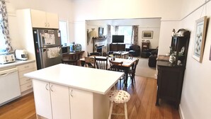 A compact kitchen with white cabinets, a central island, and a dining area with wooden chairs. - Yea Fig Tree House. Three bedroom plus study comfortable family home. (Yea)