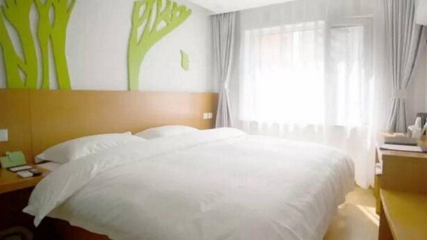 A hotel room with a large bed, a wooden headboard, a nightstand, and a window with curtains. - Vatica Chaoyang the East of Railway Station Xinhua Road Hotel (Chaoyang)