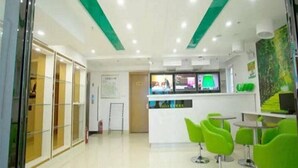 A modern office space with a reception area, green chairs, and a white reception desk. - Vatica Chaoyang the East of Railway Station Xinhua Road Hotel (Chaoyang)