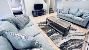 A modern living room with a grey sofa, a wooden coffee table, and a TV on a stand. - Great location! Short walk to the beach, 5min drive to center! A lot of capacity (Jamestown)