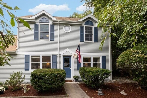 A two-story house with a front porch, a small garden, and an American flag.