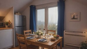 Una cocina con una mesa de comedor para dos personas, un refrigerador y una ventana con cortinas.