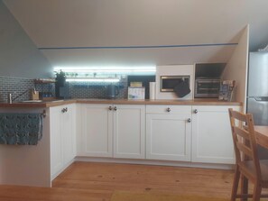 Une cuisine avec des armoires blanches, un plan de travail en bois, un four à micro-ondes et un réfrigérateur.