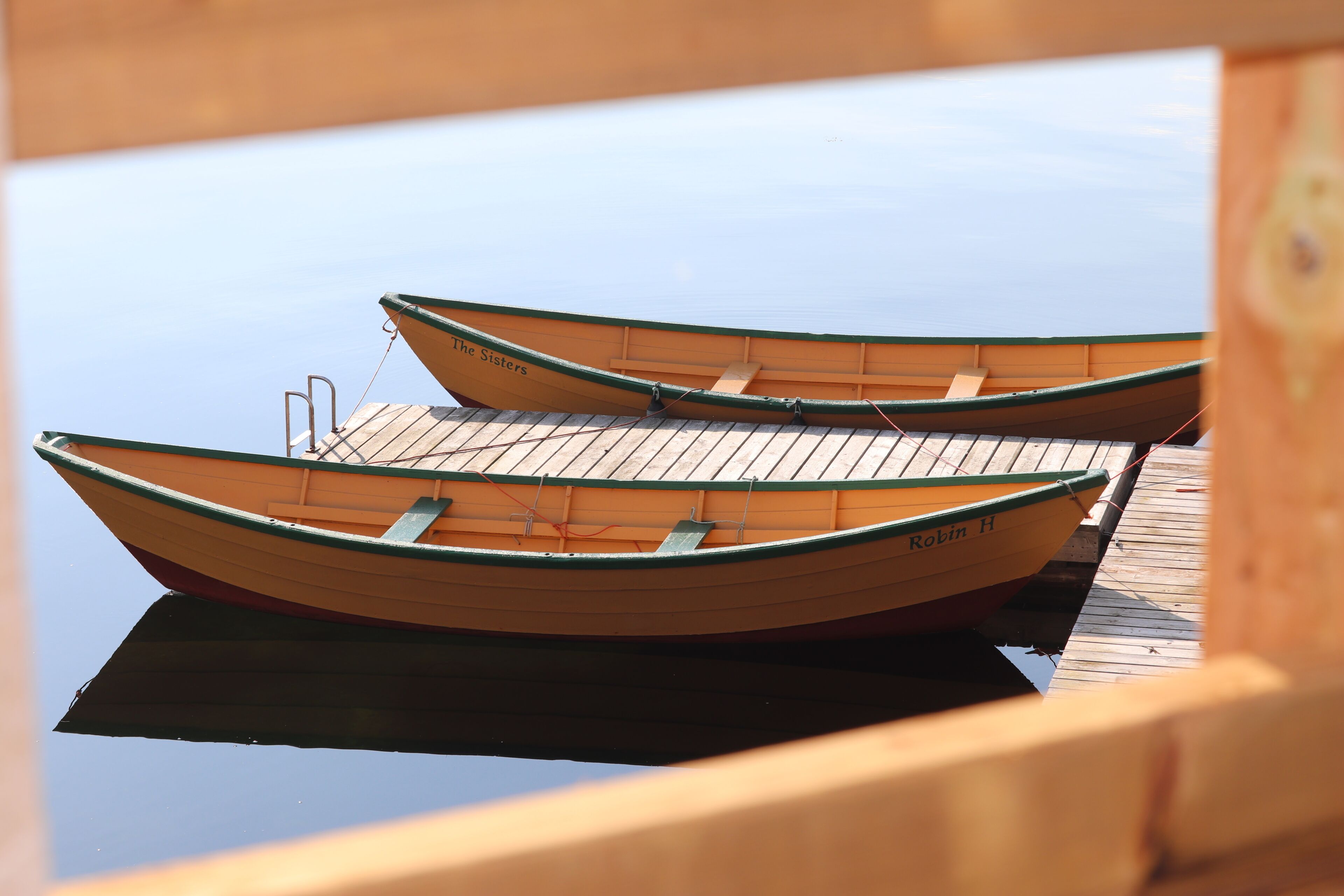 Two wooden rowboats named 'Theater' and 'Robin H' docked at a wooden pier.