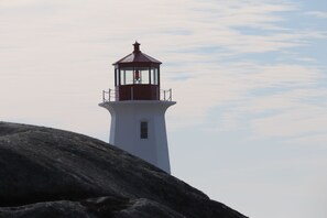A lighthouse with a white base and red top, situated on a rocky outcrop.