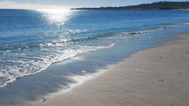 Una playa con cielo despejado, mar tranquilo y tierra a lo lejos.