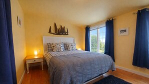 Un dormitorio con cama, mesitas de noche, ventana con cortinas, cabecera con un adorno y una alfombra oscura.