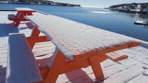 Una mesa de picnic de madera cubierta de nieve, ubicada en un muelle a orillas de un lago tranquilo.