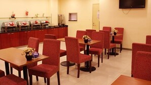Un espace repas avec des chaises et des tables à revêtement rouge, un buffet garni de différents plats et un téléviseur à écran plat fixé au mur.