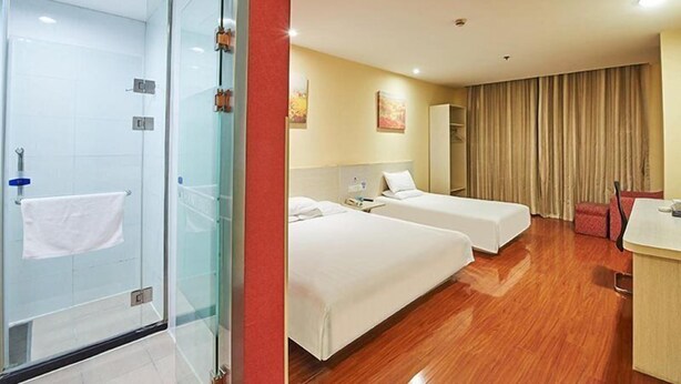 Une chambre d’hôtel avec deux lits, une douche en verre, un plancher en bois et un mur d’accent rouge.