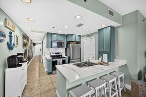 A modern kitchen with teal cabinets, stainless steel appliances, and a central island with bar stools. - Beachfront Condo at Sterling Breeze - heated pool, hot tub, gym, Wi-Fi (Panama City Beach)