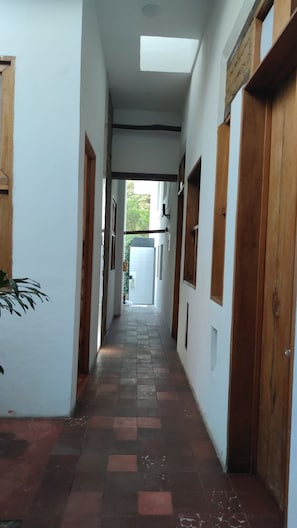 Um corredor estreito com piso de azulejos, portas de madeira e paredes brancas.