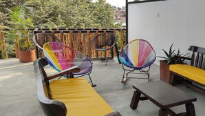 A patio with a wooden bench, two colorful chairs, and a small table.