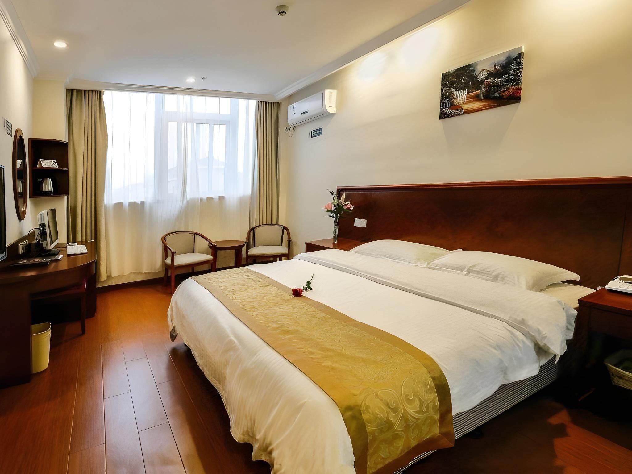 A hotel room with a large bed, two bedside tables, a desk with a chair, a TV, and a window with curtains.