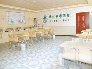Habitación de hotel con mostrador de recepción, varias mesas y sillas, una pared grande con un logotipo y un suelo estampado.