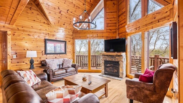 Un intérieur de chalet chaleureux, avec un revêtement en bois, une cheminée, un téléviseur et un balcon offrant une vue imprenable.