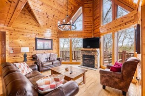 A cozy cabin interior with a wooden interior, a fireplace, a television, and a balcony with a view.