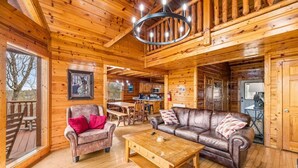 L’intérieur d’une cabane en rondins présente un salon avec un canapé en cuir marron, une table basse en bois et une cheminée.