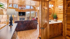 L’intérieur d’un chalet en bois comprend un espace de vie, un téléviseur, une cheminée et une cuisine équipée d’un évier et agrémentée d’une plante en pot.