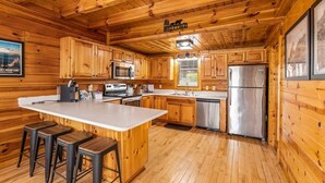 Une cuisine de style rustique, avec des éléments en bois, un îlot central, des tabourets de bar, des appareils en acier inoxydable et des armoires en bois.